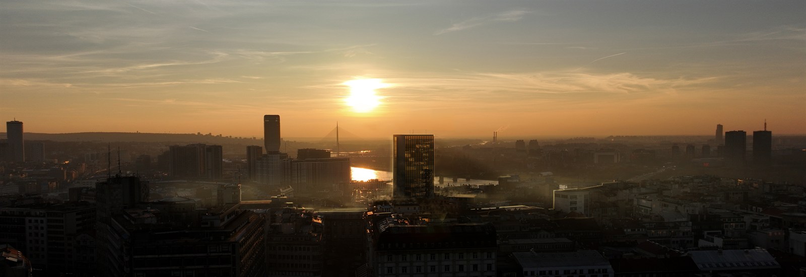 Hazy Belgrade skyline against a low sun with backlit rooftops