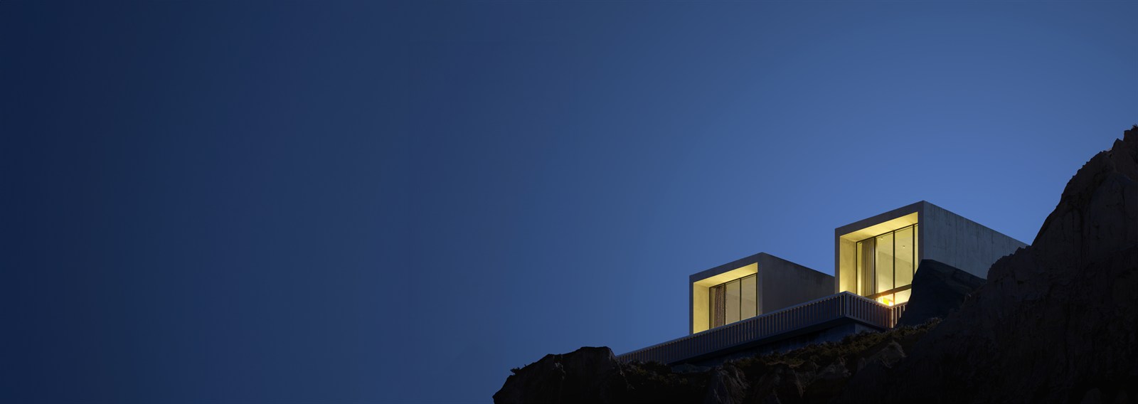 Lit cliff-top villa cantilevered over dark rock under deep blue sky