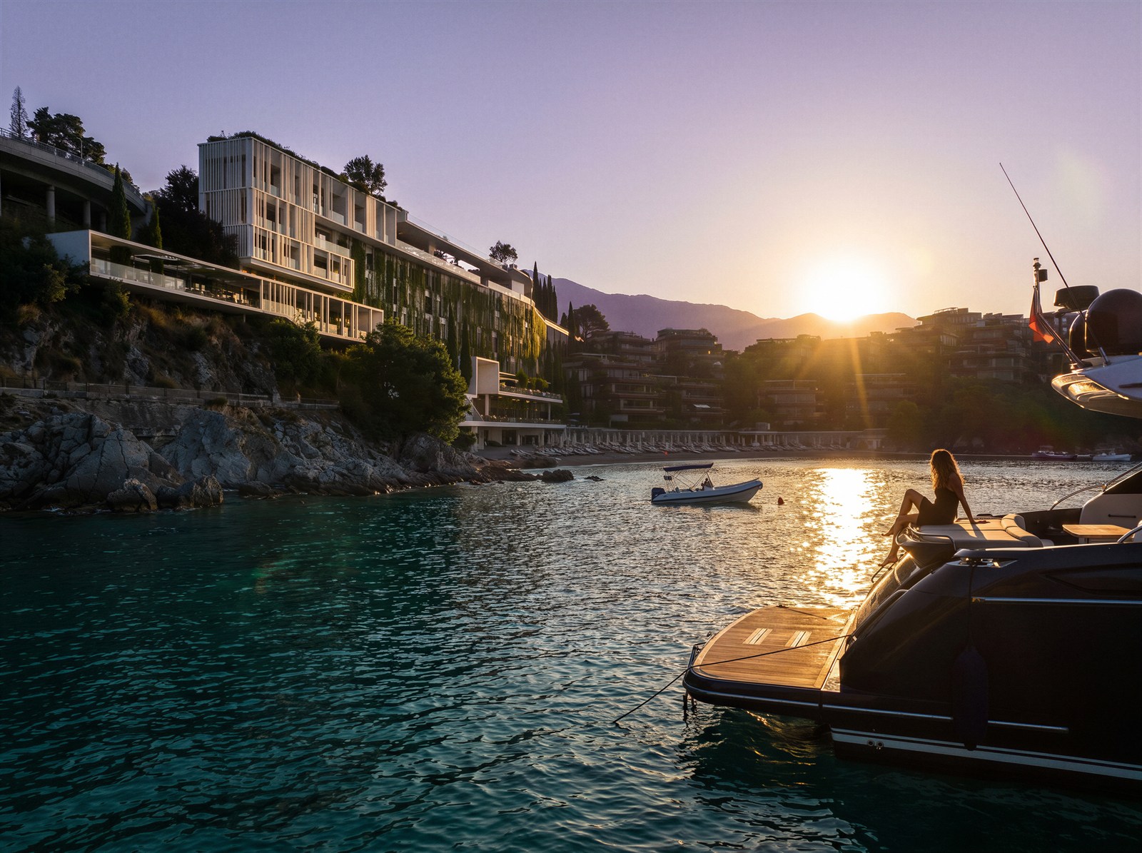 Yacht deck in the foreground, sun setting behind the cliffside resort