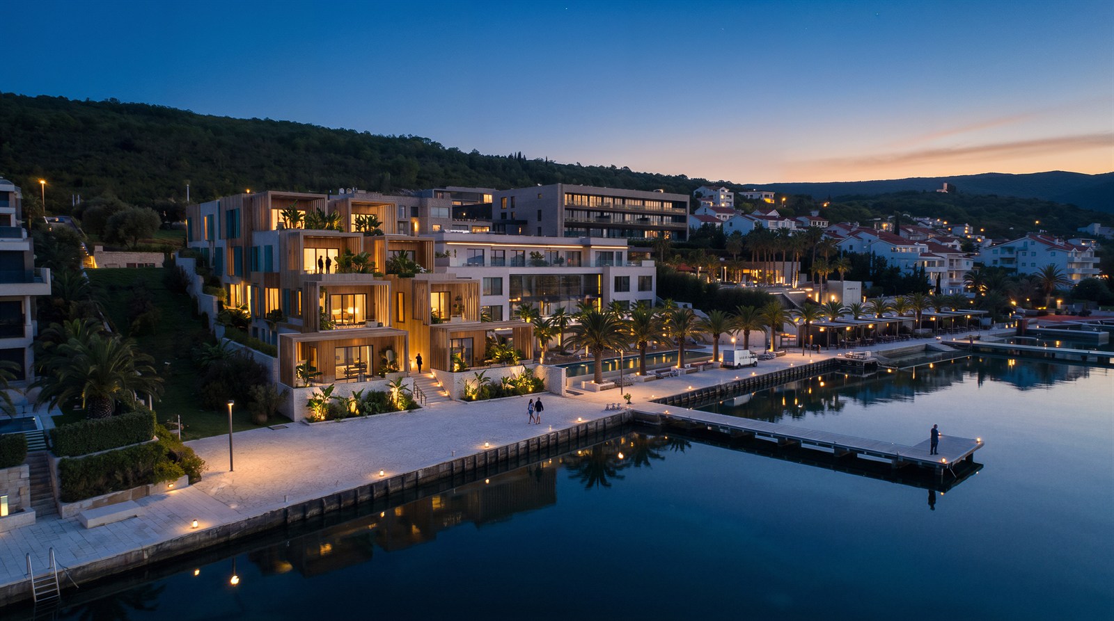 Lit marina promenade with stacked timber villas mirrored in still water