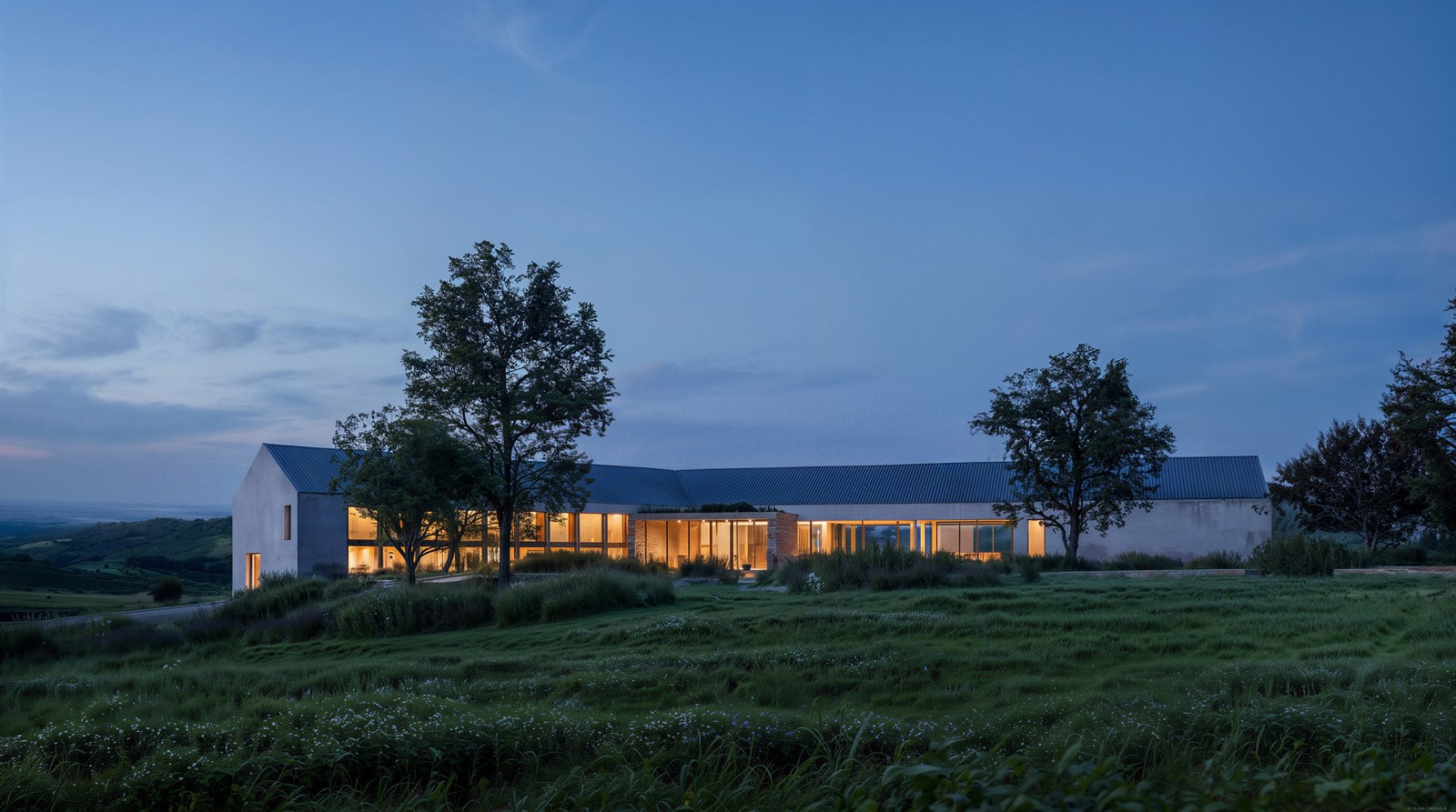 Winery glowing across meadow grass under a cool evening sky